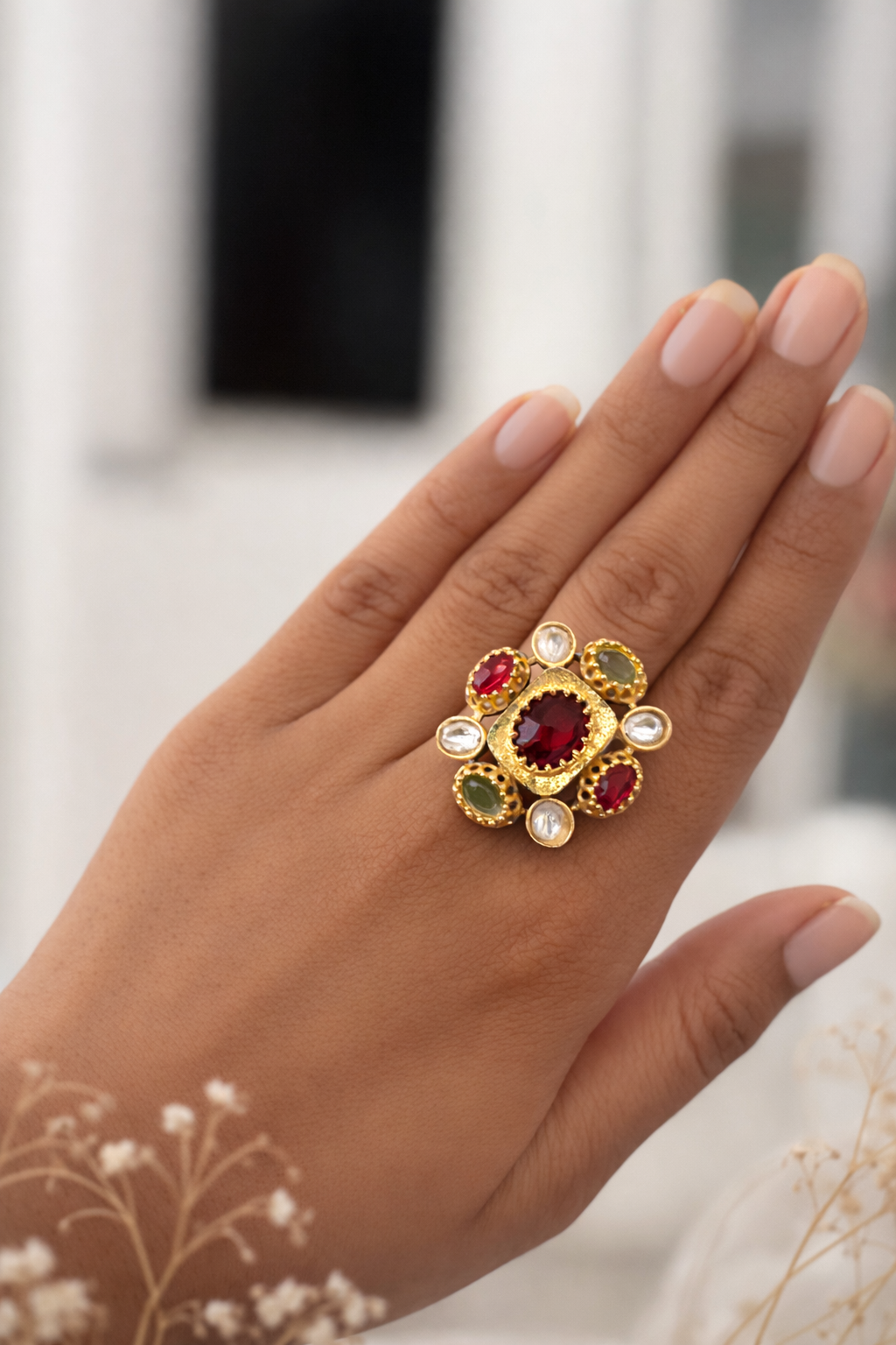 Hand wearing a decorative ring with gemstones against a blurred background