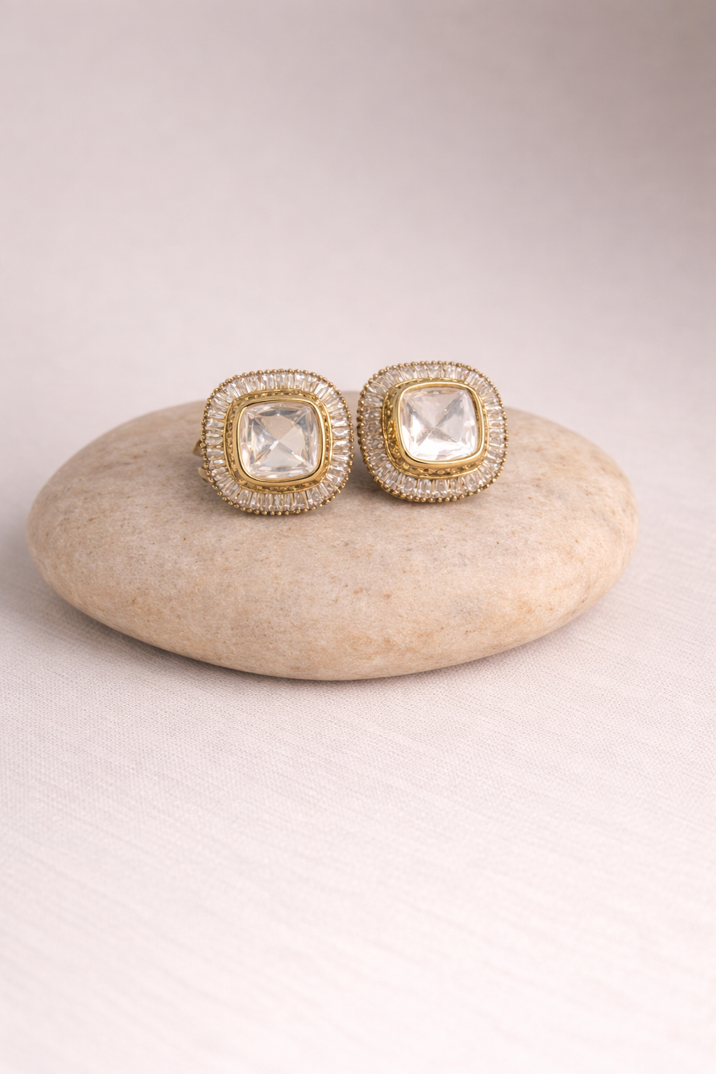 Pair of gold earrings with clear gemstones on a beige stone
