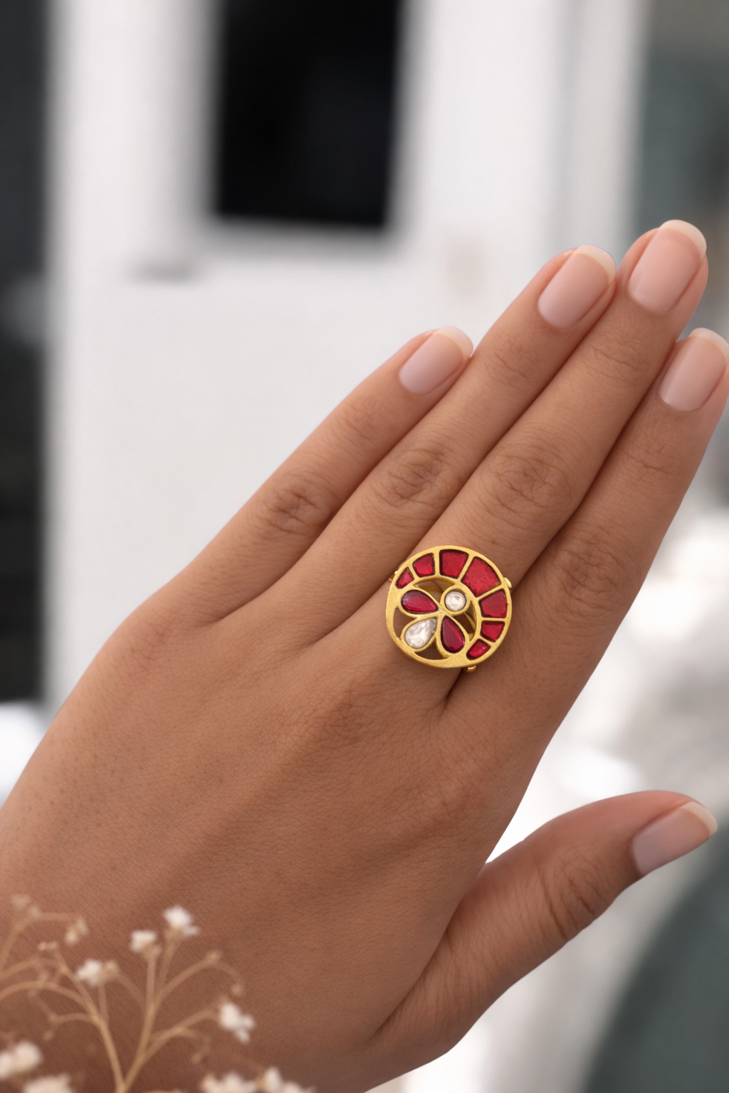 Gold ring with red and white gemstones on a hand against a blurred background
