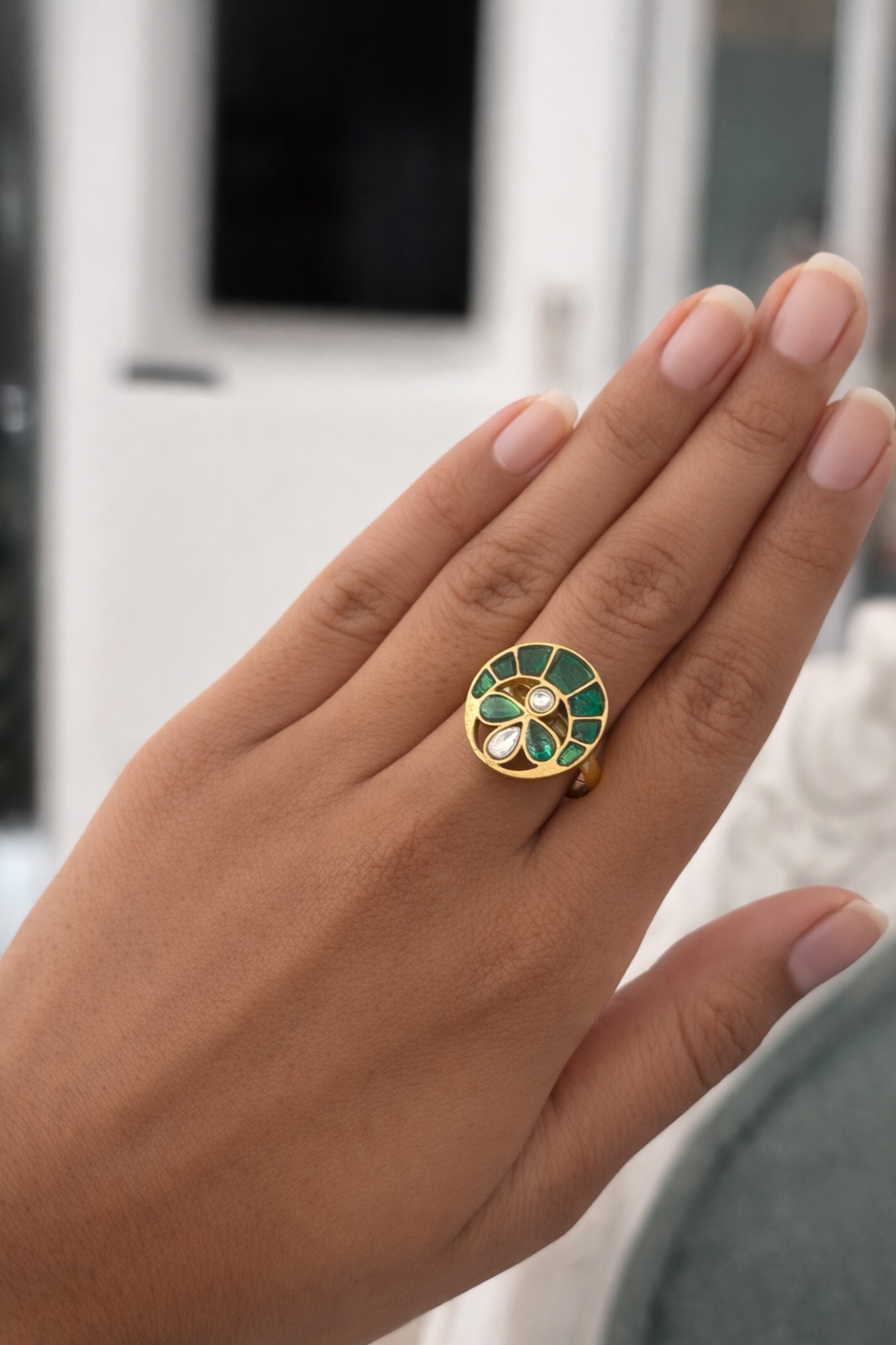 Hand wearing a decorative ring with green and gold design, blurred background