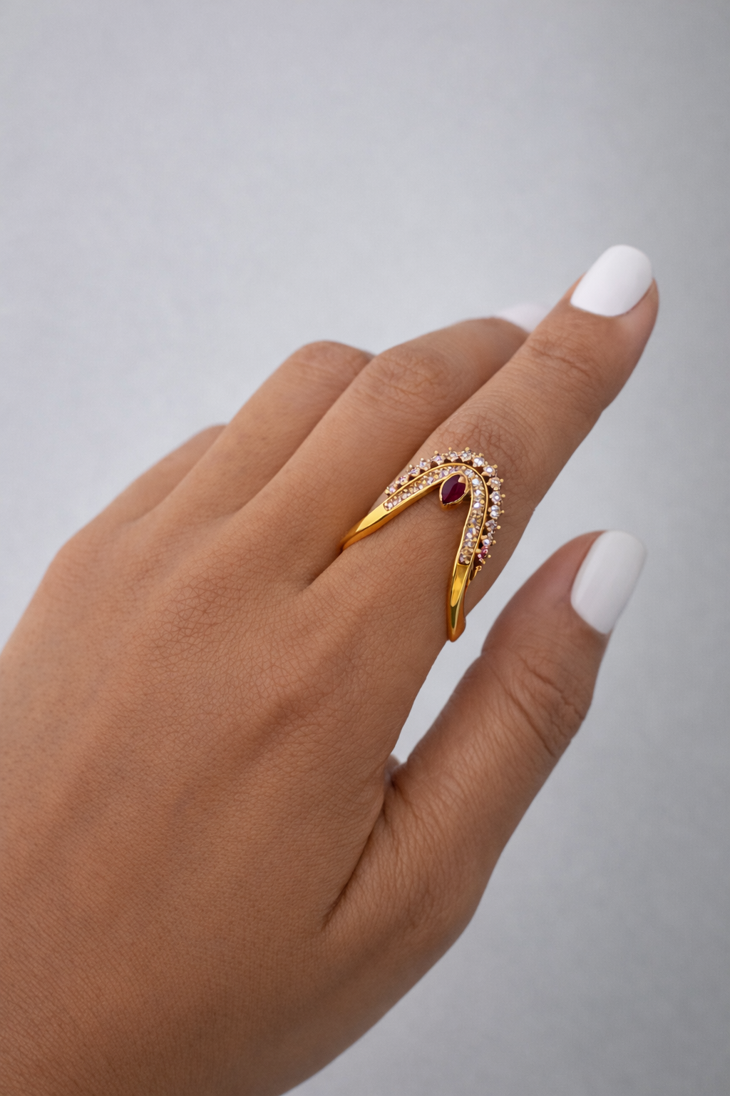 Gold ring with gemstones on a hand against a gray background