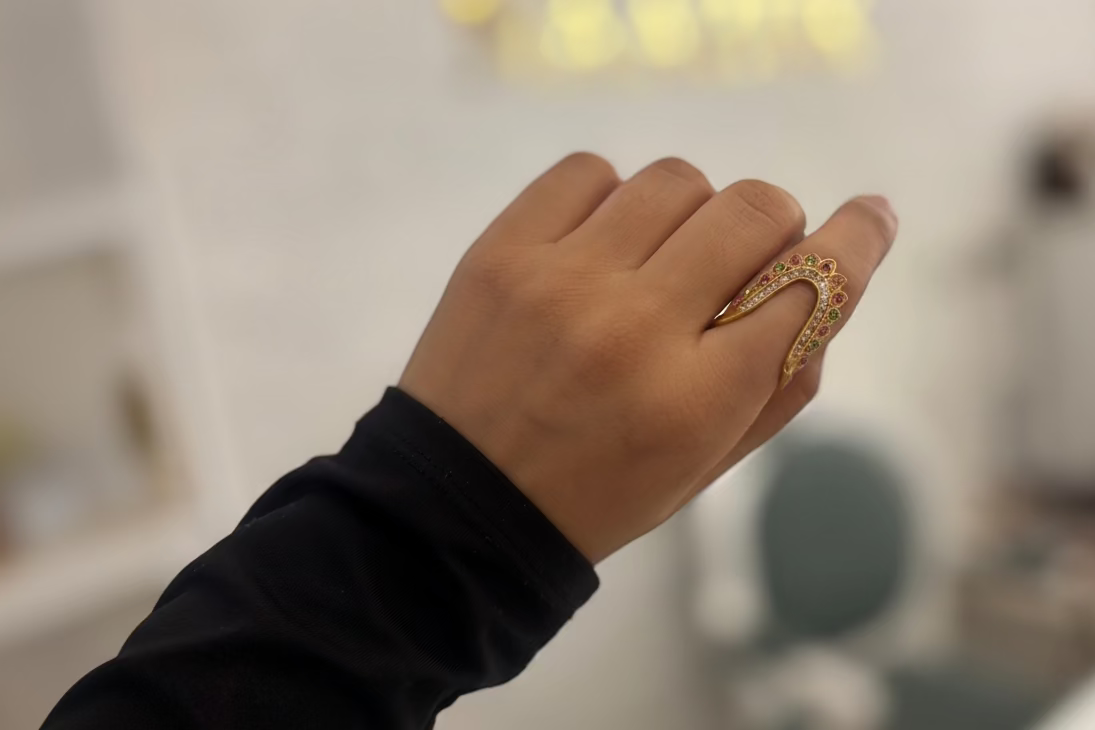 Gold ring with gemstones on a hand against a gray background