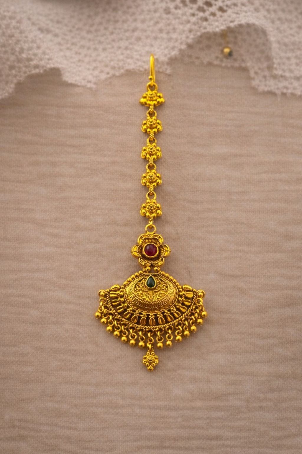 Gold pendant with red and green gemstones on a textured brown background