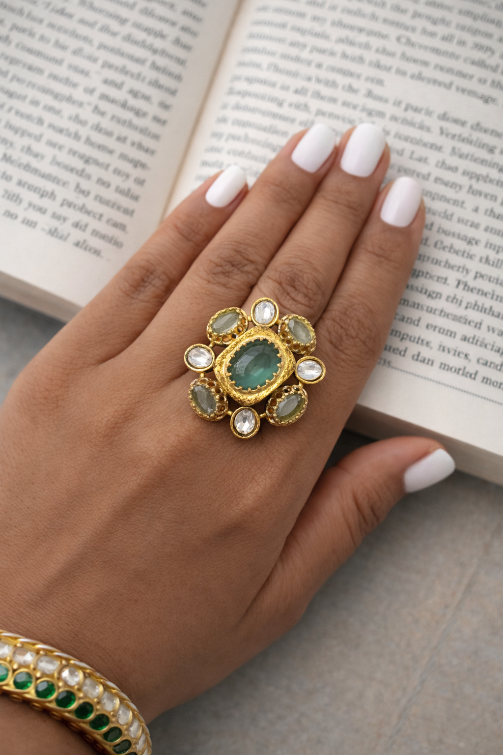 Hand wearing a decorative ring with green gemstone on an open book
